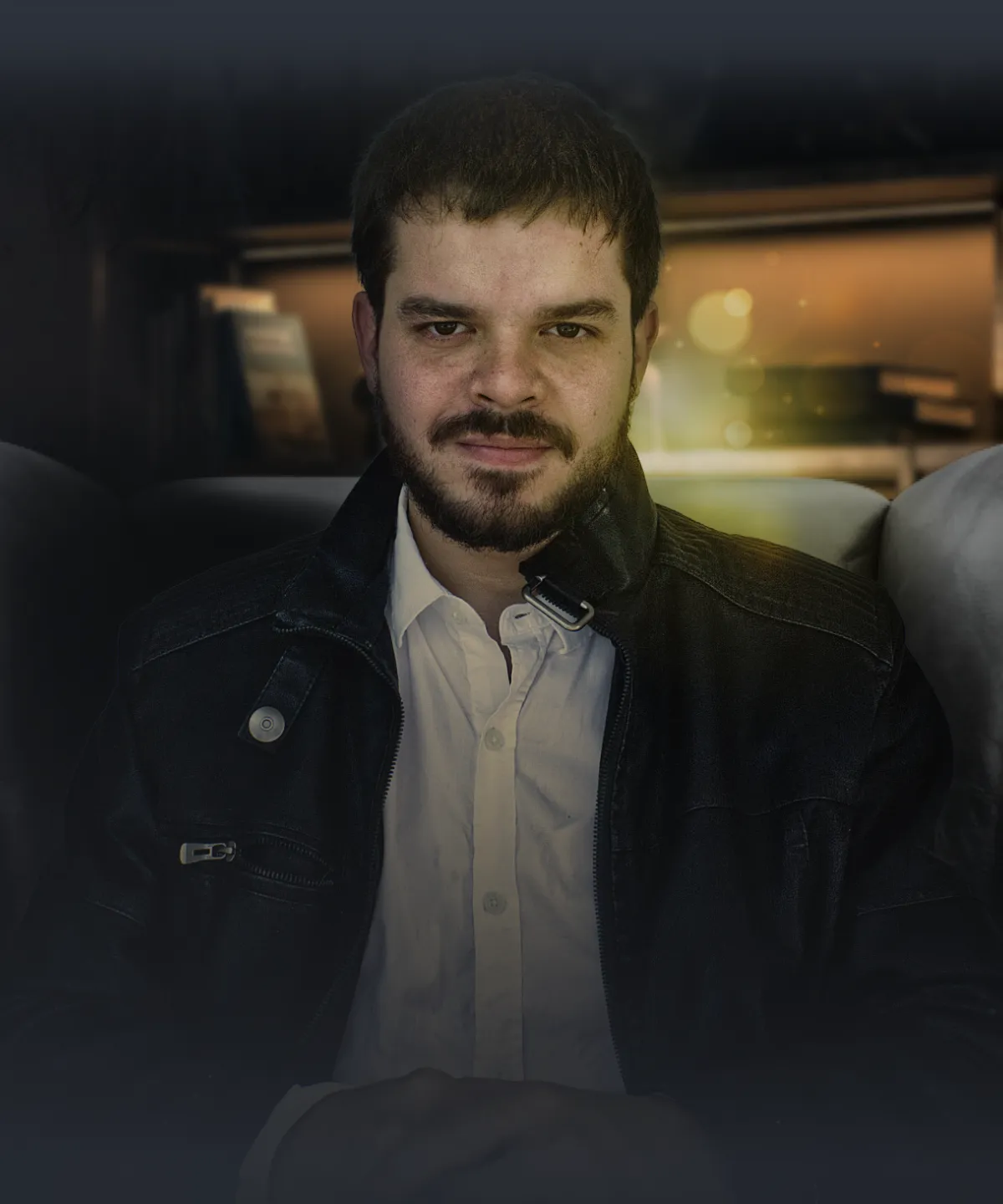 Um homem de barba e jaqueta de couro, sentado em uma poltrona em seu escritório veterinário